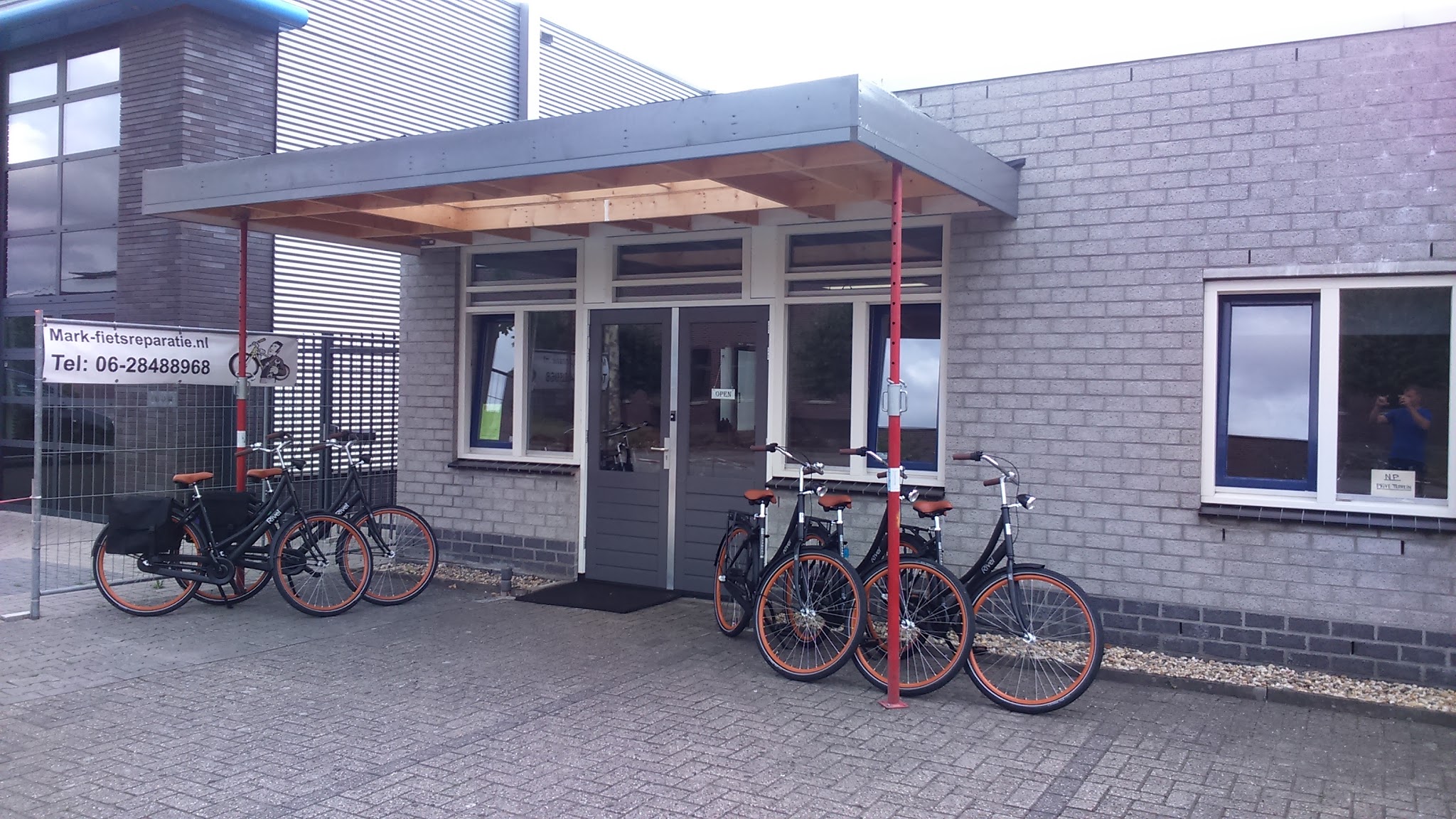 De ingang van de werkplaats met een rek nieuwe fietsen ervoor